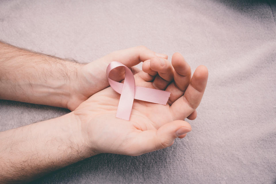 Cropped Hands Of Man Holding Breast Cancer Awareness Ribbon Over Bed