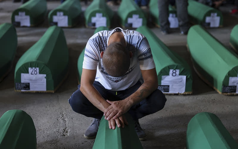 A Muslim man mourns next to the coffin of his relative, a victim of the 1995 Srebrenica genocide. Behind him are rows of other coffins covered in green fabric and marked with numbers