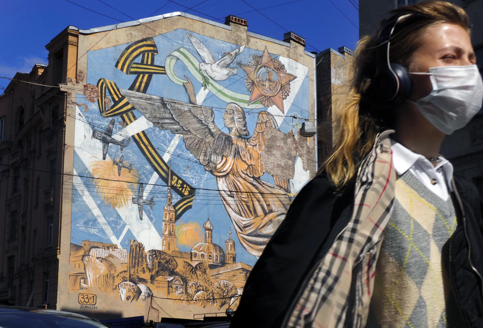 A woman wearing a face mask to protect against coronavirus walks past a graffiti dedicated to the victory of the Soviet Union in the World War II, in St.Petersburg, Russia, Monday, May 4, 2020. Victory Day, marking the 75th anniversary of defeating of Nazi Germany will be celebrated on May 9 in Russia. (AP Photo/Dmitri Lovetsky)