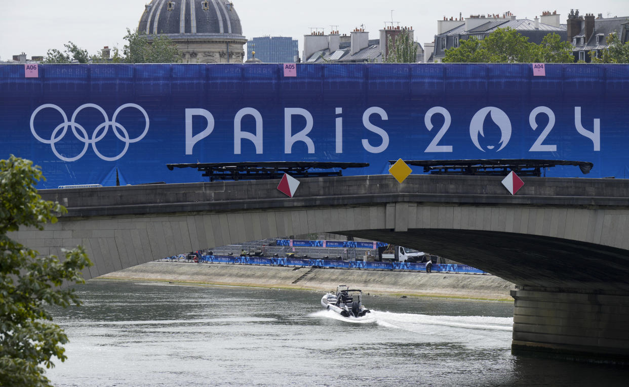 A boat beneath a bridge with a sign reading: Paris 2024.