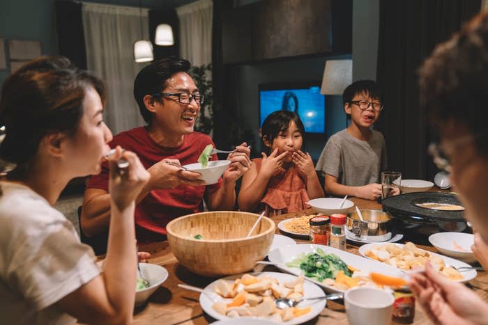 A family of five, including a mother, father, and three children, dines together at a table filled with various foods. They are all smiling and enjoying their meal