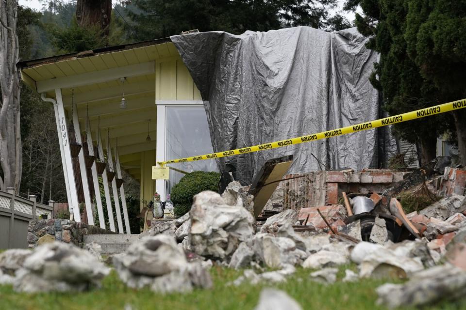 A light-yellow color home damaged by an earthquake, partly covered with tarp, with rubble around it