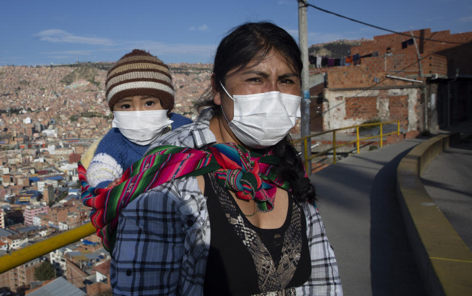 Una mujer lleva a su hijo al mercado durante un cierre ordenado por el gobierno, que limita a los residentes a comprar por la mañana como medida para ayudar a contener la propagación del nuevo coronavirus en La Paz, Bolivia, el lunes 6 de abril de 2020. (AP Foto/Juan Karita)