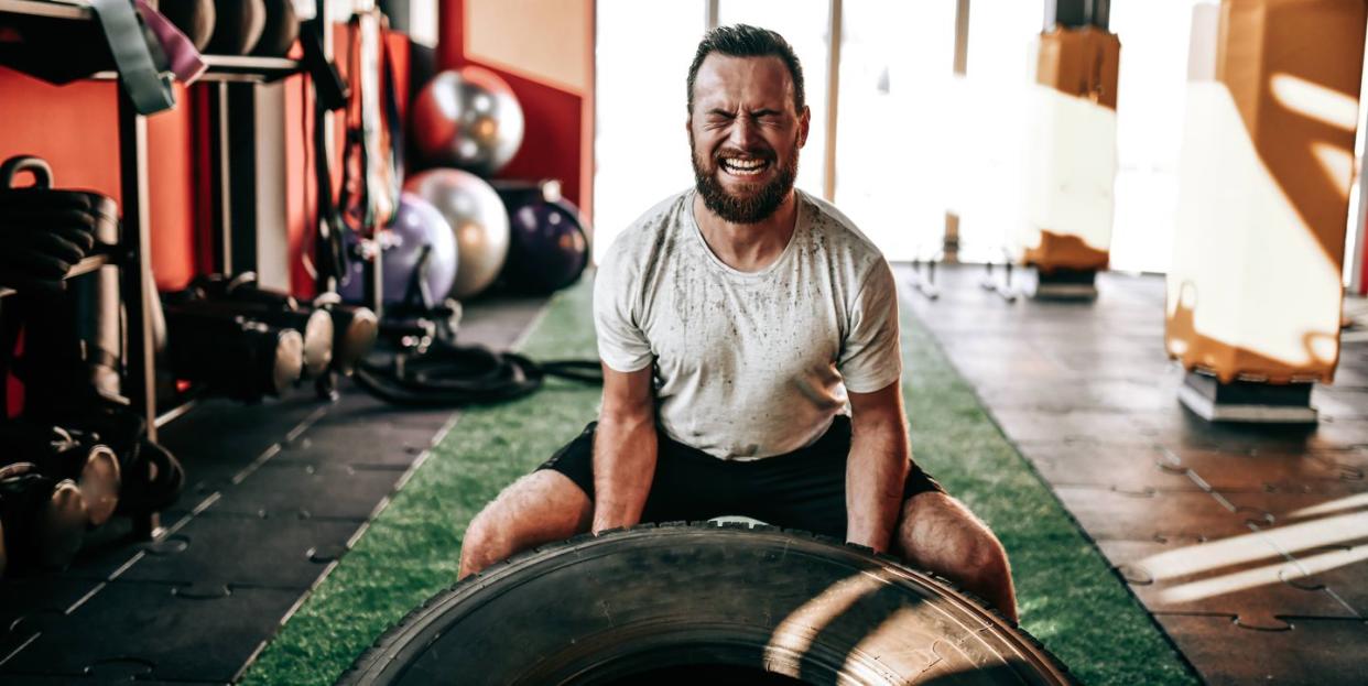 male athlete wincing with effort during truck tire gym workout