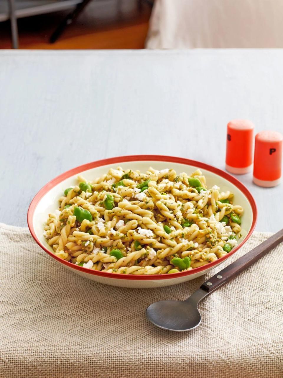 fava bean pasta salad with garlic scape pesto in a red rimmed bowl