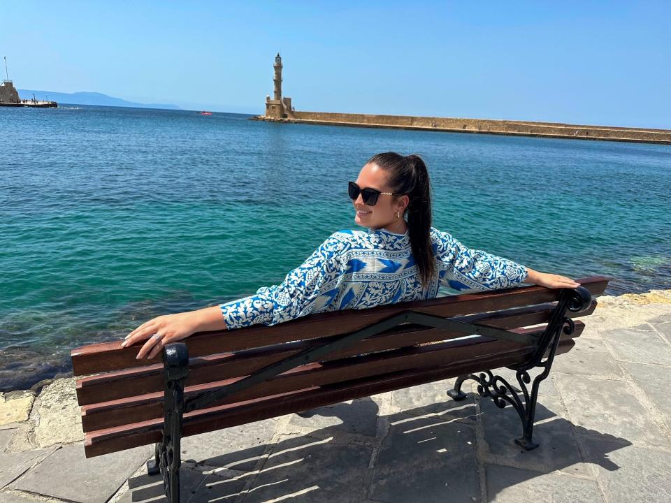 The author with arms stretched on a bench in front of blue waters, smiling