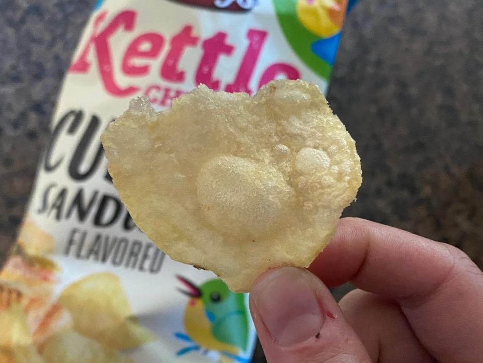 hand holding a chip outside of a bag of aldi cuban sandwhich flavored chips