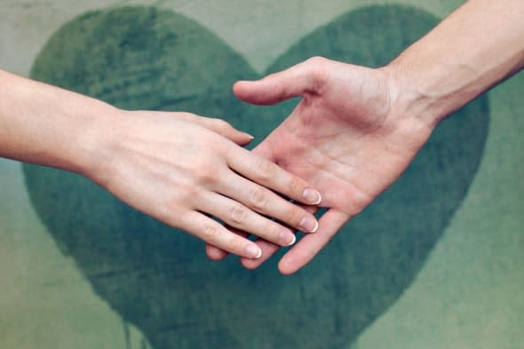 Man touching woman's hand with a heart painted wall in background