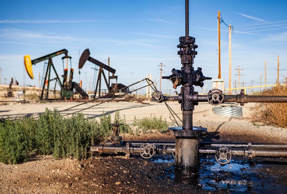 An oil pumpjack with a leaky wellhead is dripping with oil into a puddle along the side of a road through the Midway-Sunset oil field in Kern County, California.