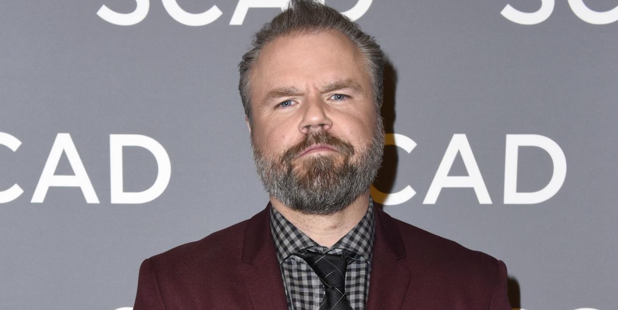 tyler labine posing for a picture in a maroon jacket and checkered shirt and tie