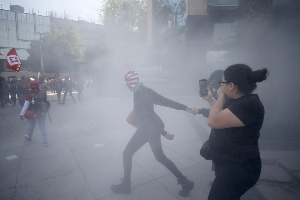 Demonstrators are surrouned by a cloud of tear gas during an International Women's Day march in Mexico City, Sunday, March 8, 2020. Protests against gender violence in Mexico have intensified in recent years amid an increase in killings of women and girls.(AP Photo/Rebecca Blackwell)