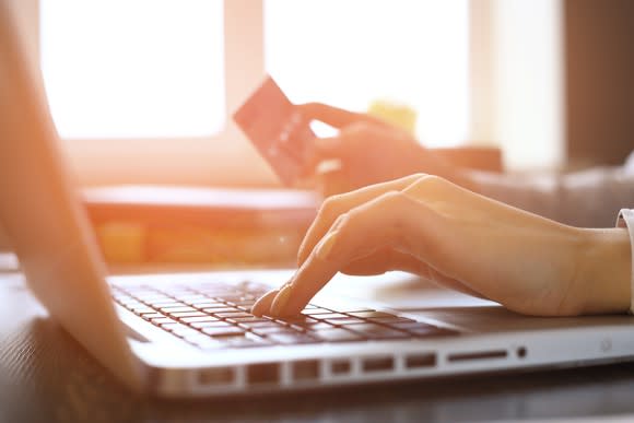 A woman's hand hovers over keyboard while other holds credit card.