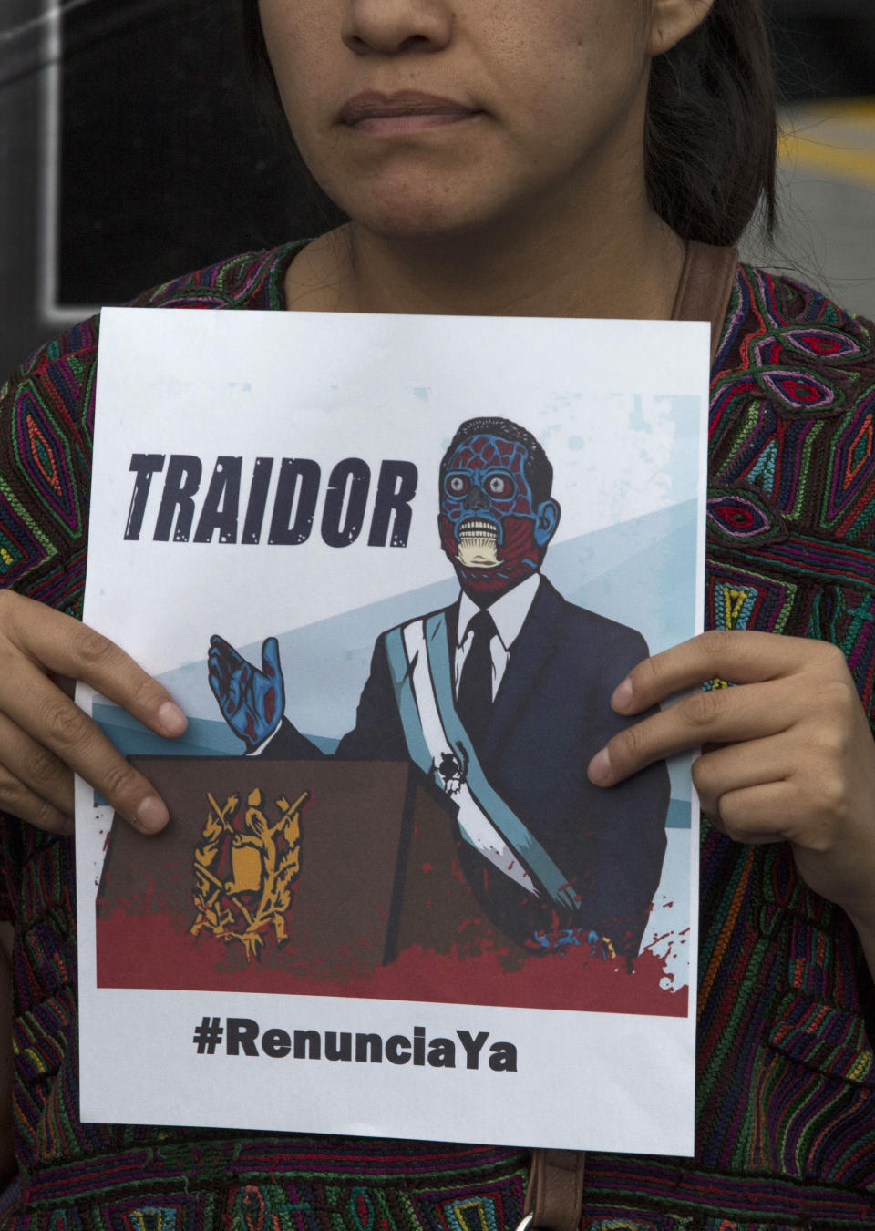 A woman holds a poster showing a cartoon image of Guatemalan President Jimmy Morales with the word "traitor" ,during a press conference organized by civil society groups in front of the Constitutional Court in Guatemala City, Friday, July 26, 2019. The Trump administration signed an agreement with Guatemala Friday that will restrict asylum applications to the U.S. from Central America. (AP Photo/ Oliver de Ros)