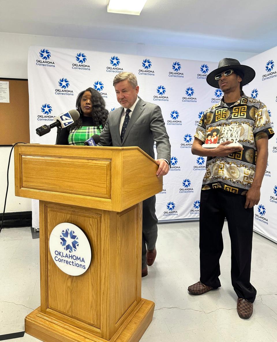 Oklahoma Attorney General Gentner Drummond reads a statement on behalf of murder victim Janet Moore on 4 April 2024, while standing between Moore's son, Phillip Zachary, Jr., and niece Morgan Miller-Perkins at the Oklahoma State penitentiary in McAlester, Okla., following the execution of Michael Dewayne Smith. The 41-year-old was sentenced to die for killing Moore and Sharath Pulluru in separate shootings in February 2002 (AP)