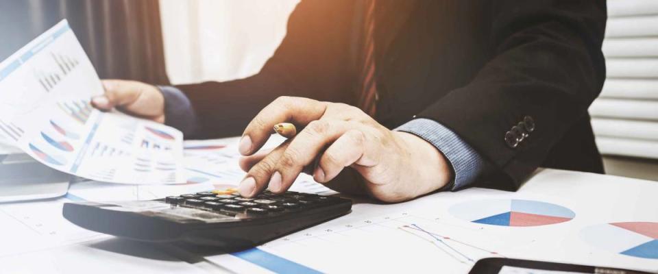 Close up of man using calculator, looking at a bunch of charts and graphs on papers on his desk.