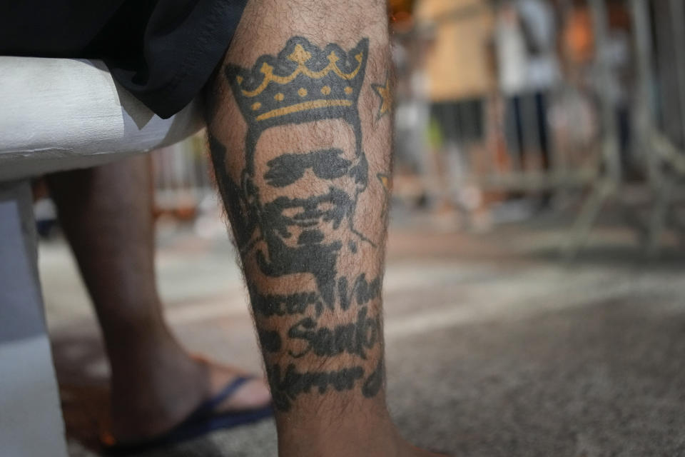 A soccer fan with a tattoo depicting the late Brazilian soccer legend Pele sits outside the Vila Belmiro stadium where his body lies in state for his wake in Santos, Brazil, early Tuesday, Jan. 3, 2023. (AP Photo/Matias Delacroix)