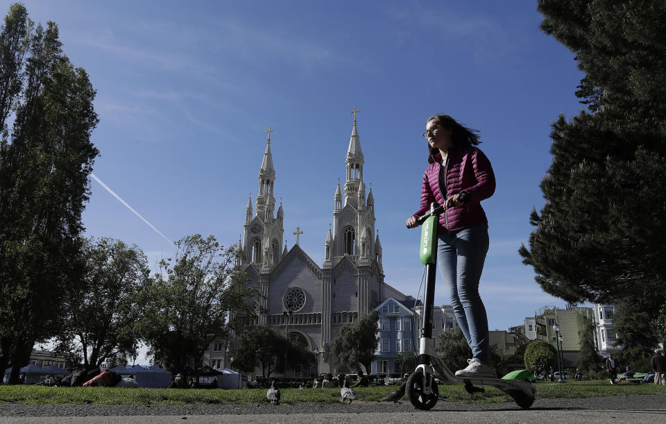 FILE - In this April 17, 2018 file photo, a woman rides a motorized scooter in Washington Square Park in San Francisco. Tired of San Francisco sidewalks being used as a testing ground for delivery robots, drones, and electric scooters, city supervisors will vote Tuesday, Dec. 10, 2019, to set up a new regulatory office that would require businesses to get permits before trying out new technology that uses public space. (AP Photo/Jeff Chiu, File)