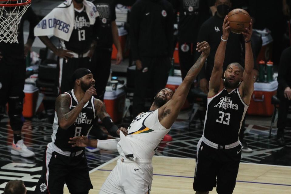 The Clippers' Nicolas Batum, right, grabs a rebound away from the Jazz's Derrick Favors, middle, as Marcus Morris looks on.