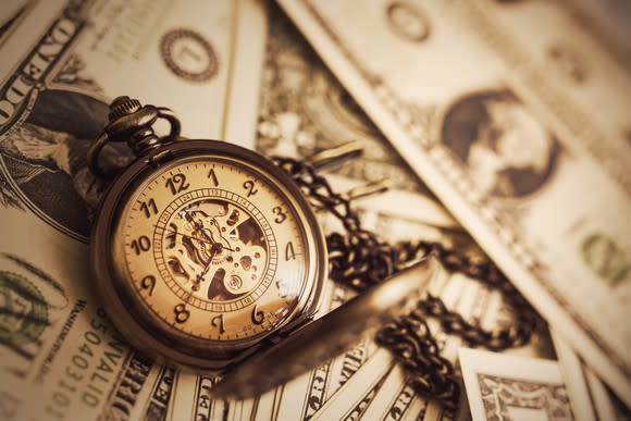 Traditional pocket watch on a chain sitting on top of paper currency