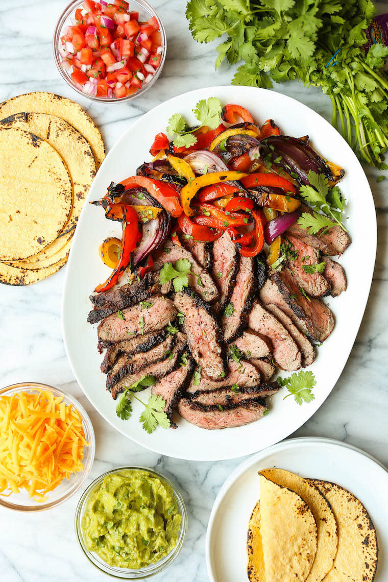 Fajitas served family style with bowls of cheese, guacamole, tortillas, and a big plate of grilled steak with peppers and onions.