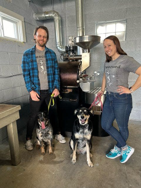 Ben and Brittany Essig stand with their rescued pups Bourbon, left, and Pabst in front of the roaster in their coffee business Rescued Roasters, which donates 10% of its profits to animal rescue organizations.