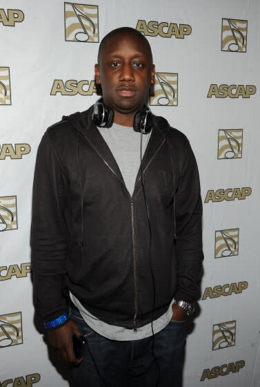 A man in a dark hoodie poses with a headphones draped around his neck