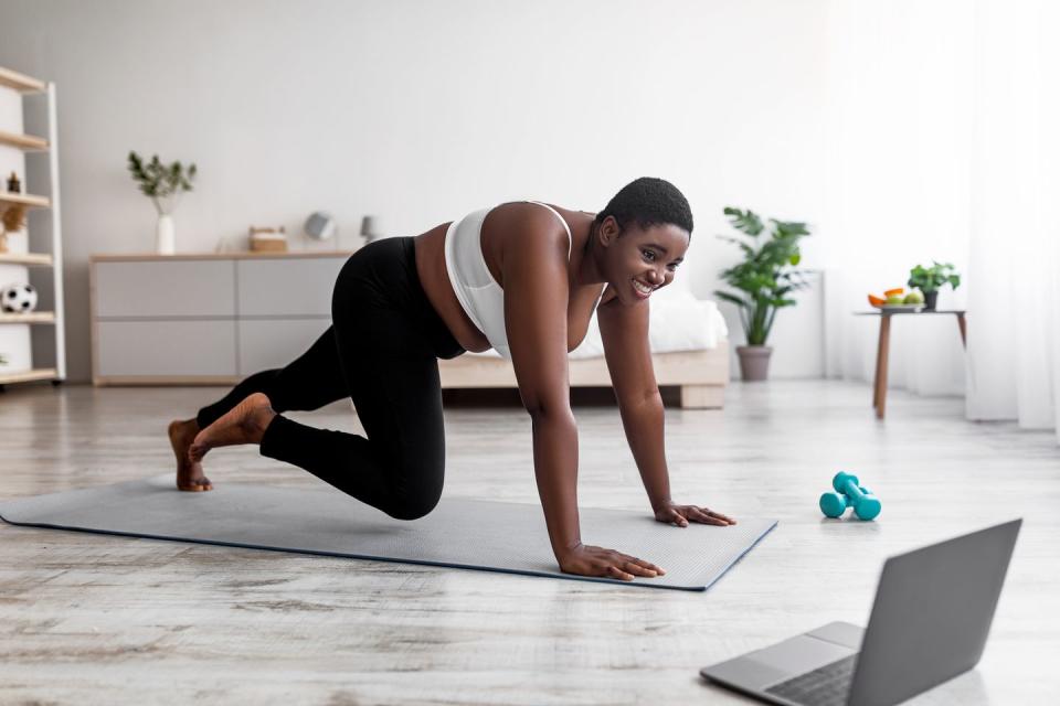 plus size afro woman having strength workout, following web tutorial on laptop, running with hands on floor at home