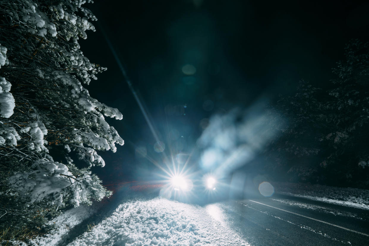  Light from the headlights of a car on a winter road surrounded by snowy forest at night. 