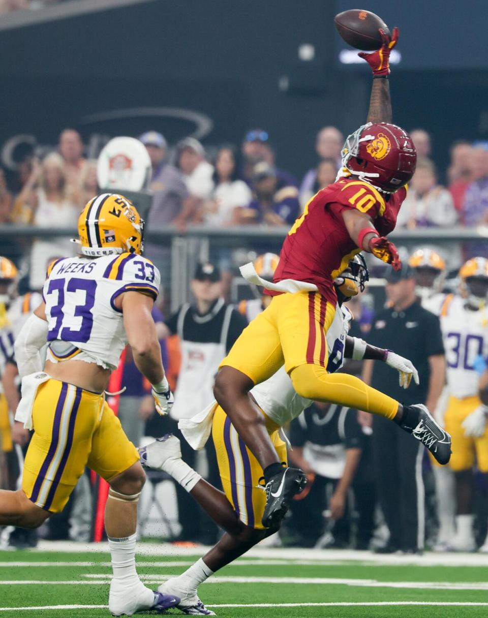 USC receiver Kyron Hudson leaps, leans back and extends one hand in the air to catch a pass between two LSU players.