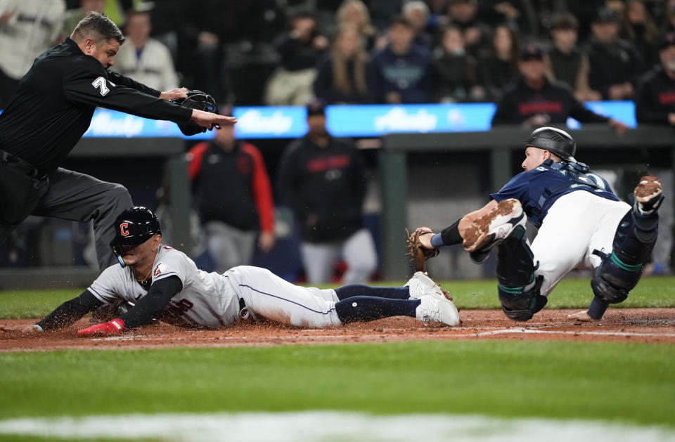 Cleveland Guardians' Andres Gimenez scores past Seattle Mariners catcher Cal Raleigh, right, as umpire Jordan Baker makes the call the second inning of a baseball game Friday, March 31, 2023, in Seattle. (AP Photo/Lindsey Wasson)
