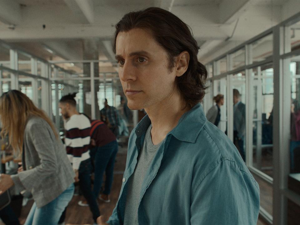 jared leto as adam neumann in wecrashed, standing in an office and looking pensively to the side