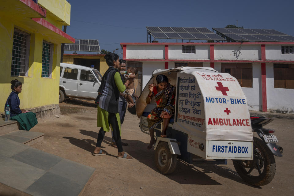 Basanti Warda, left, a health worker, holds one-year-old Dilesh as his mother Phagni Poyam, 23, a nine months pregnant woman, disembarks from a motorbike ambulance as she arrives for a checkup at a hospital in Orchha in central India's Chhattisgarh state, Nov. 16, 2022. These ambulances, first deployed in 2014, reach inaccessible villages to bring pregnant women to an early referral center, a building close to the hospital where expectant mothers can stay under observation, routinely visit doctors if needed until they give birth. Since then the number of babies born in hospitals has doubled to a yearly average of about 162 births each year, from just 76 in 2014. The state has one of the highest rates of pregnancy-related deaths for mothers in India, about 1.5 times the national average, with 137 pregnancy related deaths for mothers per 100,000 births. (AP Photo/Altaf Qadri)