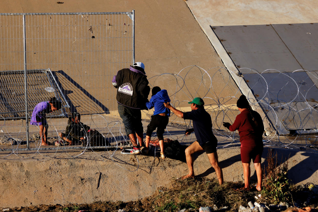 Several asylum-seeking migrants try to cross barbed wire to get into the United States.