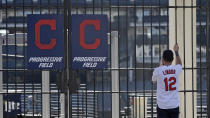 FILE - In this March 26, 2020, file photo, Daniel Clemens looks into the empty ballpark at Progressive Field in Cleveland. Clemens, a season ticket holder, had tickets for the opening day baseball game between the Cleveland Indians and the Detroit Tigers. With no games being played, recent sports headlines have centered around hopes and dreams — namely, the uncharted path leagues and teams must navigate to return to competition in the wake of the pandemic. (AP Photo/Tony Dejak, File)