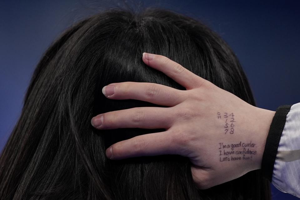 Japan's Satsuki Fujisawa runs her fingers through her hair and a message to herself written on her hand "I'm a good curler. I have confidence. Let's have fun!" during a women's curling match against China at the Beijing Winter Olympics Monday, Feb. 14, 2022, in Beijing. (AP Photo/Brynn Anderson)