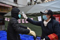 Una mujer revisa la temperatura a un ciclista que porta una mascarilla en la ciudad de Wuhan, en el centro de China, el viernes 21 de febrero de 2020. (Chinatopix via AP)