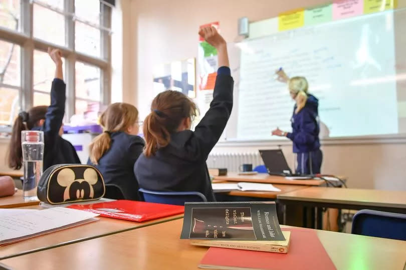 Classroom where pupils raise their hands. A Teacher stands at a projected whiteboard