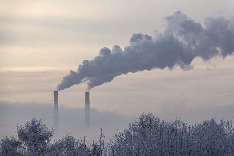 Two smoke stacks release thick clouds of smoke on the horizon.