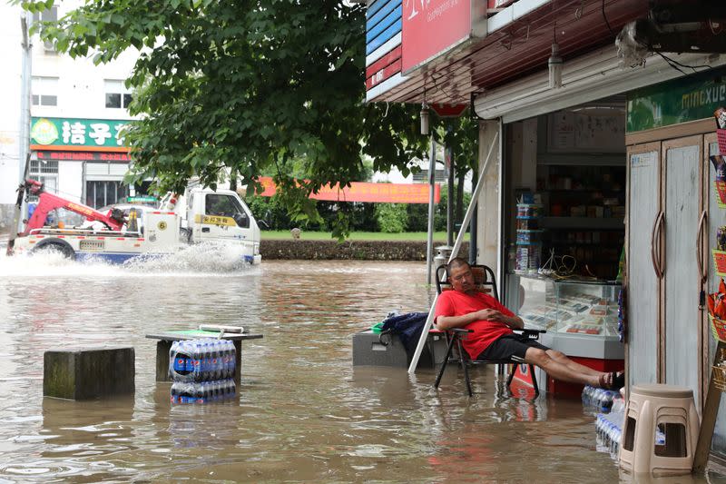 Man rests outside a flooded shop after heavy rainfall led to flooding in Quzhou