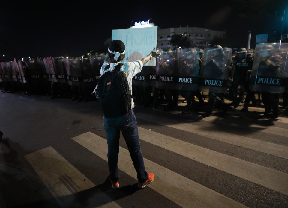 A protester holds up a sign in front of riot police Saturday, March 20, 2021 in Bangkok, Thailand. Thailand's student-led pro-democracy movement is holding a rally in the Thai capital, seeking to press demands that include freedom for their leaders, who are being held without bail on charges of defaming the monarchy. (AP Photo/Sakchai Lalit)