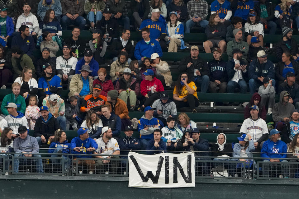 Fans sit in front of a "WIN" sign in the outfield during the second inning of a baseball game between the Seattle Mariners and the Texas Rangers, Friday, Sept. 29, 2023, in Seattle. (AP Photo/Lindsey Wasson)