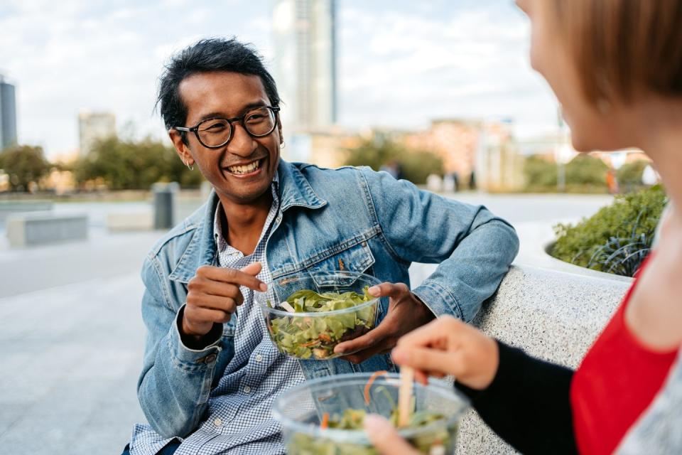 young couple eating a salad and talking on the bench in milan