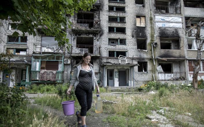 A Ukrainian woman collects water from a well in a civilian district amid destruction in Lyman City