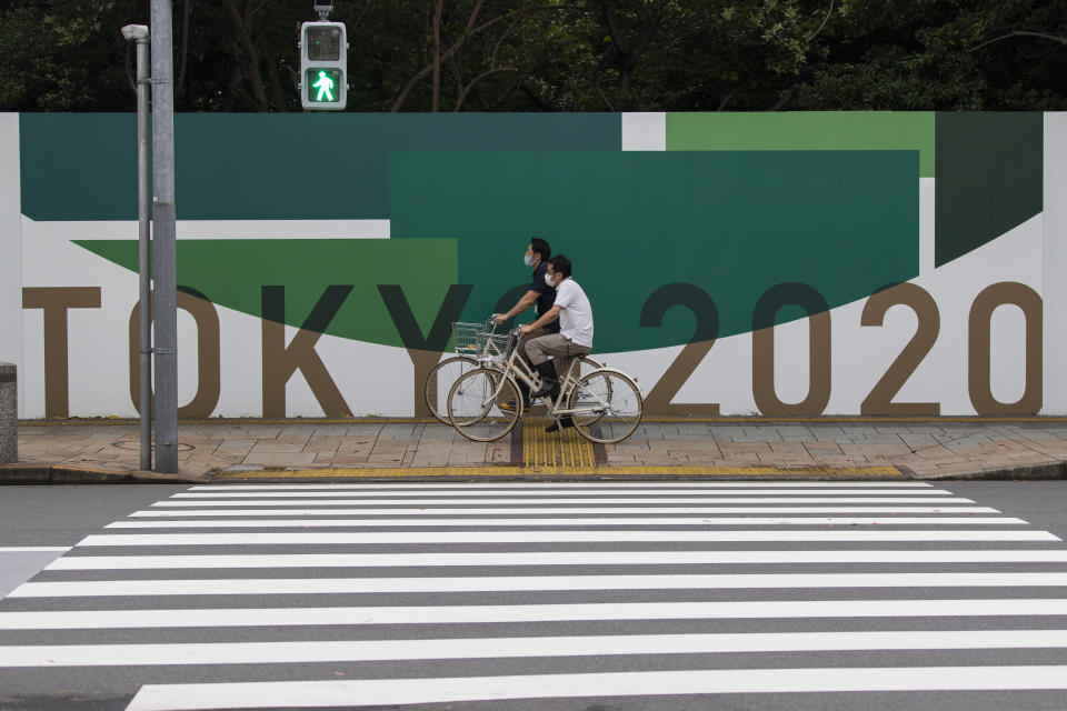 Men wearing face masks ride bicycles along the wall installed to close off a park being prepared for the Olympics and Paralympics Games in Tokyo on Thursday, July 1, 2021. (AP Photo/Hiro Komae)