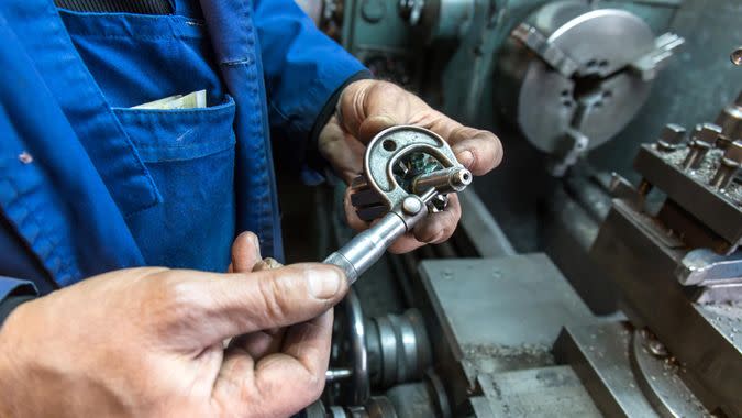 worker man hand measuring with micrometer in a workshop beside the turning machine.