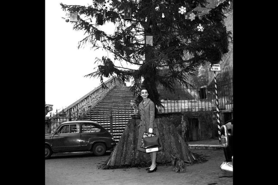 <p>Audrey Hepburn looks chic and sophisticated in Switzerland over the holidays in 1950. The actress wore a gray tweed coat dress with a simple black handbag, as she and her Yorkshire Terrier pose under a Christmas tree. </p>