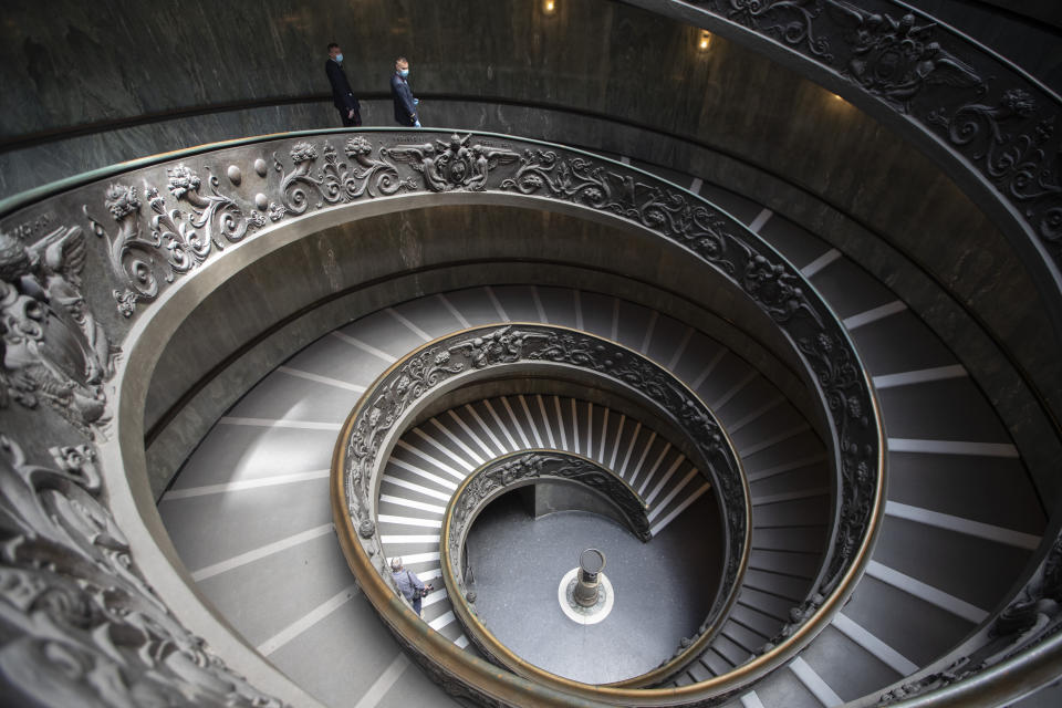 Museum employees, wearing masks to prevent the spread of coronavirus, walk down a staircase designed by Giuseppe Momo in 1932, inspired by the original Bramante staircase designed by Renaissance architect Donato Bramante, as the Vatican Museum reopened, in Rome, Monday, June 1, 2020. The Vatican Museums reopened Monday to visitors after three months of shutdown following COVID-19 containment measures. (AP Photo/Alessandra Tarantino)