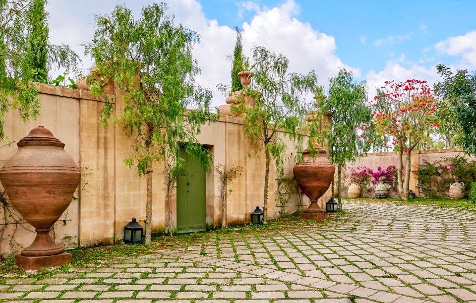 Pepper trees and a pair of 17th-century vessels once used to hold olive oil frame an exterior door.