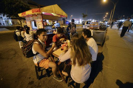 Estudiantes universitarios cenan en Lima el 18 de marzo de 2014 en uno de los "restaurantes de agachados", puestos informales de comida en la vía pública que ofrecen los platos más típicos de Perú por menos de dos dólares (AFP | Cris Bouroncle)