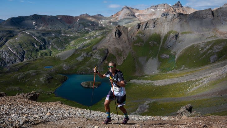 Woman hikes in the mountains with a blue lake in the background and mountains